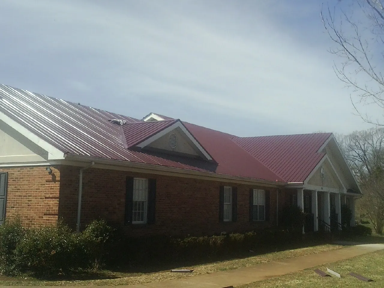 Red metal roof with gabled entries on a long brick building, from a Hail Damage Roof Repair job in Hobgood
