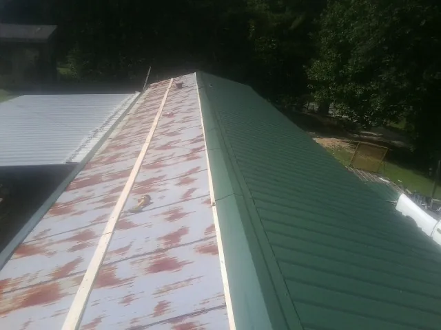 Old rusted panels beside newly installed green metal roofing — Wind Damage Roof Repair by Roofing Brothers in Hobgood