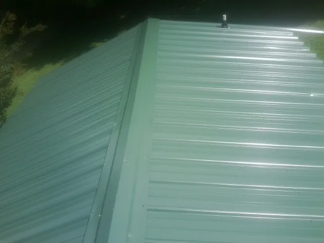 New green metal panels meeting at the ridge of a roof — Flat Roof Repair work by our crew in Hobgood