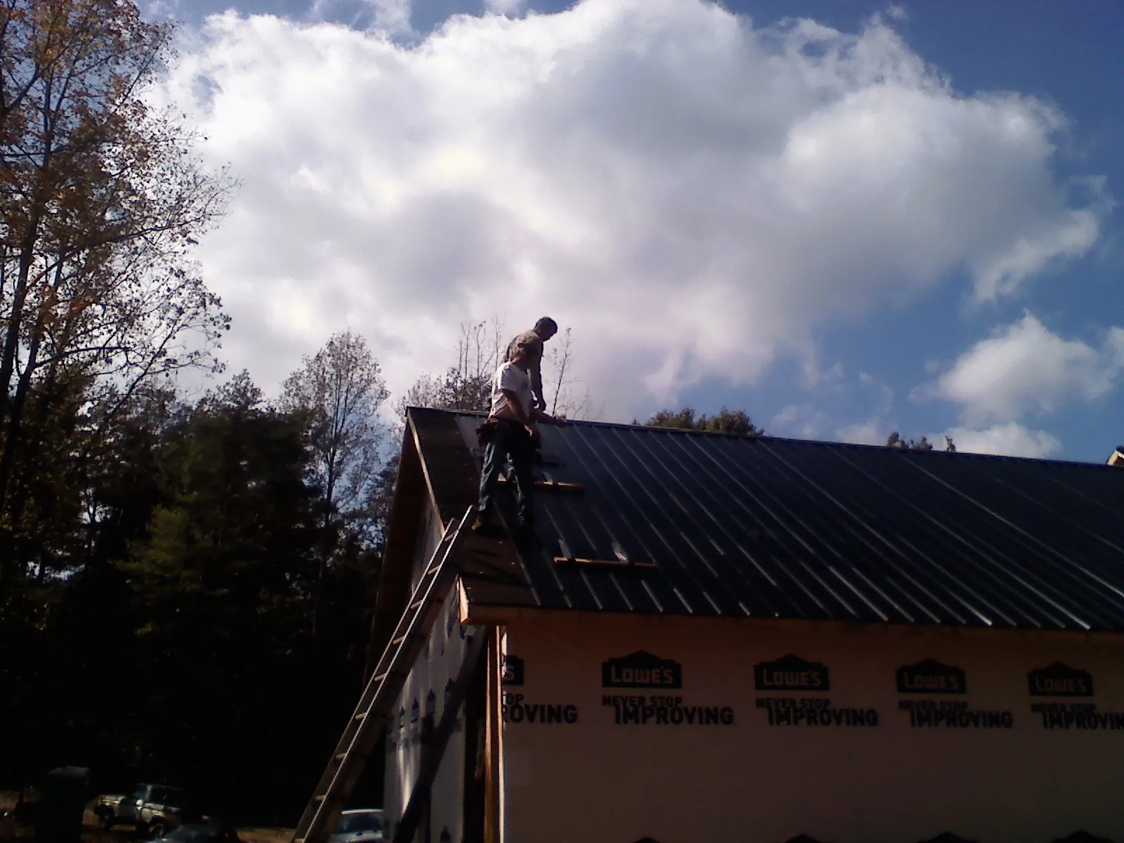 Roofer fastening dark metal panels high against a cloudy sky, from a Roof Inspection job in Hobgood