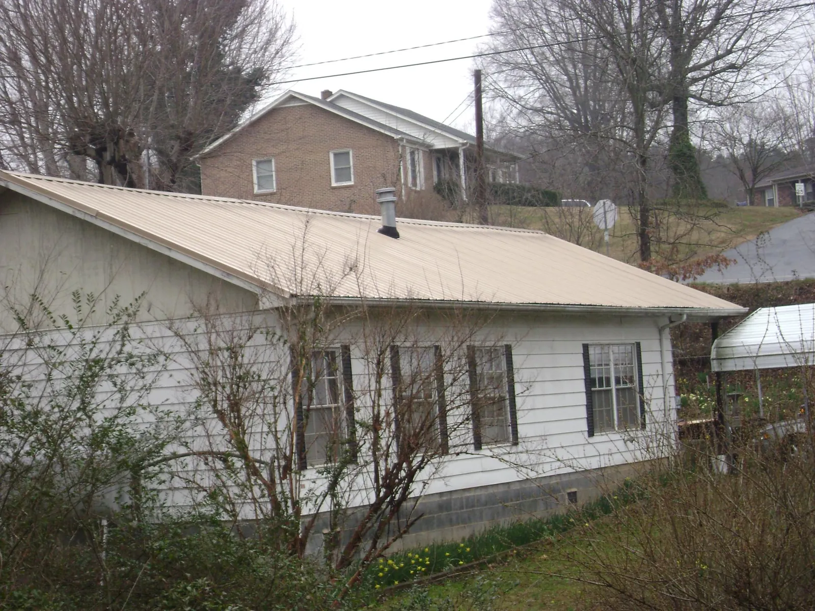 Tan metal roof on a white sided house set into a hillside — Commercial Roofing by Roofing Brothers in Hobgood