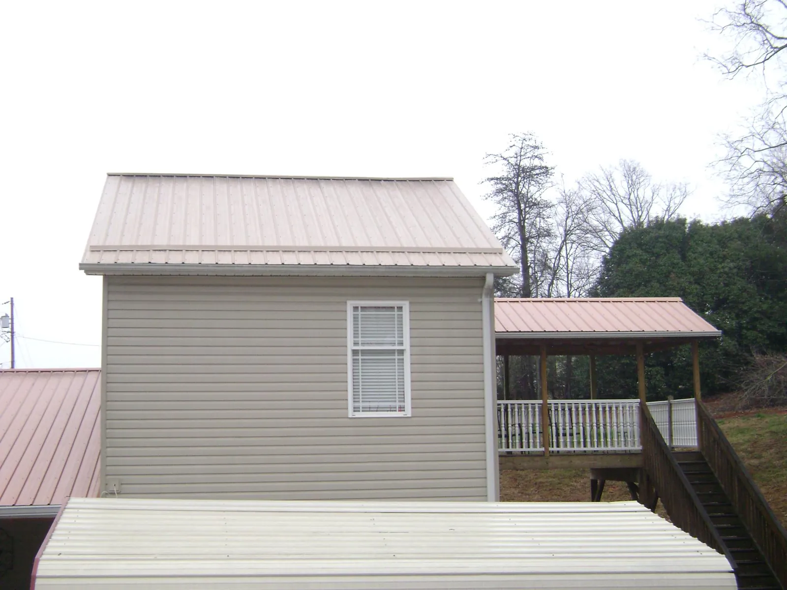 Tan metal roofs on a two story addition and attached porch, from a Roof Replacement job in Hobgood